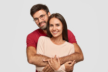Lovely Couple Have Warm Cuddle, Pose For Family Portrait, Smile Joyfully, Have Good Relationships. Affectionate Brother Embraces His Sister Isolated Over White Wall. Girlfriend And Boyfriend Have Date