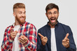 © WHstudio Leushin N - Joyful males make gun gesture choose something, have toothy smile and happy expressions, dressed in fashionable outfit, model against white background, express choice. Hipsters gesture indoor