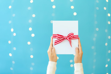 Canvas Print - Person holding a Christmas gift box on a shiny light blue background