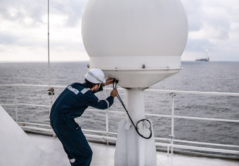 Marine service technician or serviceman repairing VSAT terminal on deck of vessel or ship. He is checking connection cables