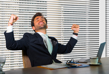 lifestyle corporate company portrait of young happy and successful business man working excited at modern office sitting by window computer desk celebrating victory