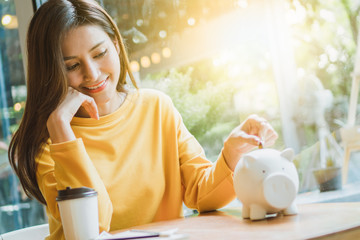 Asian woman saving money and dropping coin to piggy