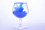 Fototapeta Paryż - Blue paint in water in a crystal glass on a white background