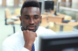 © ty - Portrait of successful African-American businessman sitting at desk with computer in office.