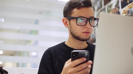 Close-up portrait of male programmer, developer working on a laptop and phone. Develops a mobile application