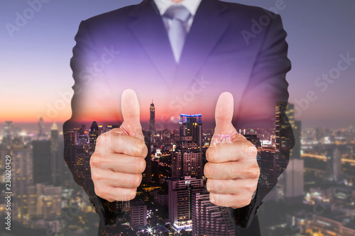 Fotomural Double exposure of businessman give a two thumbs up for compliment and cityscape