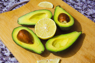 tasty ripe green avocado with brown bone and yellow lemon on a wooden board