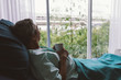 © saksit - Senior man on a hospital bed alone in a room looking through the hospital window. Elderly patient