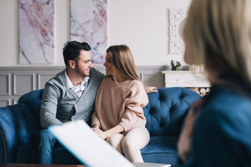 Young happy couple after successful therapy session with family psychologist, sitting on sofa embracing.