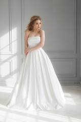 Beautiful blonde woman in beige powdery silk wedding dress posing in studio room