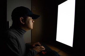 side view of man hacker sit at the computer monitor. in the dark room.