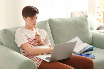 Wall Mural - Cute teenager boy using laptop while doing homework indoors