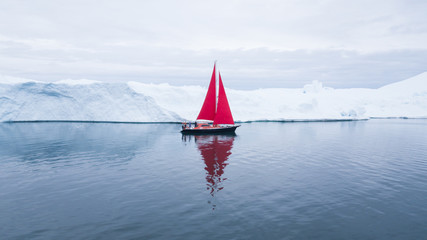 Wall Mural - beautiful red sailboat in the arctic next to a massive iceberg showing the scale - aerial view as vi