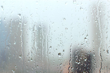 Rain drops on window glasses surface with cloudy background.