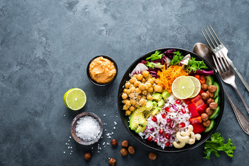 Healthy vegetarian Buddha bowl with fresh vegetable salad, rice, chickpea, avocado, sweet pepper, cucumber, carrot, pomegranate and nuts closeup