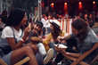 © Yakobchuk Olena - Portrait of cheerful hipster girl in hat feeding boyfriend with fork while sitting on folding chair. Blurred bearded man and girl in glasses eating and smiling