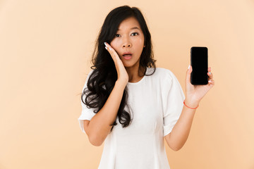 Shocked asian woman posing isolated over beige wall background showing display of phone.