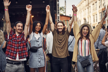 Wall Mural - Happy emotions. Portrait of young stylish people holding arms and jumping while enjoying outdoor music concert