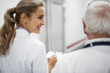 © Yakobchuk Olena - Back view portrait of beautiful young lady in white lab coat holding clipboard and chatting with old therapist. They heading to patient room