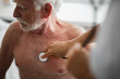 © Yakobchuk Olena - Cropped portrait of shirtless bearded gentleman looking away with serious expression while doctor listening his breath with stethoscope
