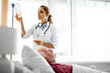 © Yakobchuk Olena - Waist up portrait of young woman in white lab coat checking intravenous drip in hospital room. Blurred old man lying in bed