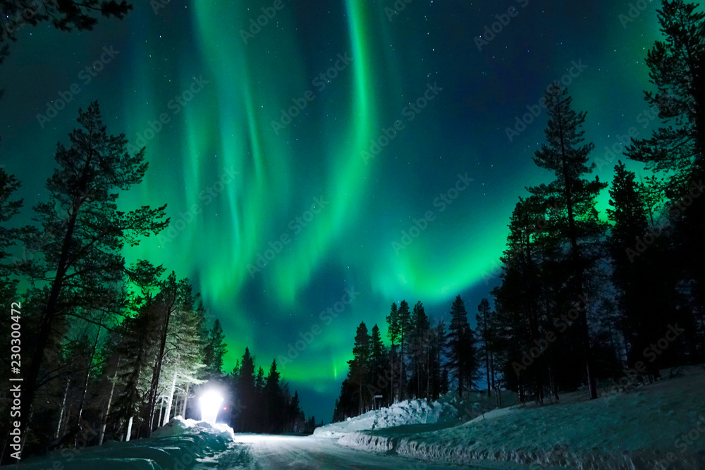 Bright lamp shining on the empty snowy road just as the northern lights appear. - obrazy, fototapety, plakaty 