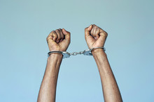 Close-up. Arrested African Man Handcuffed Hands. Prisoner Or Arrested Terrorist, Close-up Of Hands In Handcuffs. Isolated On Gray Background
