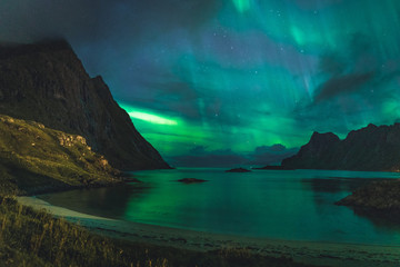  Aurora over sandy beach haukland, Kvalvika and Skagsanden with stones in Norway, Lofoten islands. Northern lights in Lofoten islands, Norway. Starry sky with polar lights. Night landscape with green