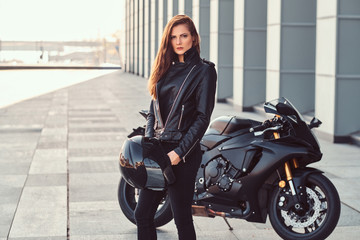 Wall Mural - A beautiful biker girl holding helmet next superbike outside a building.