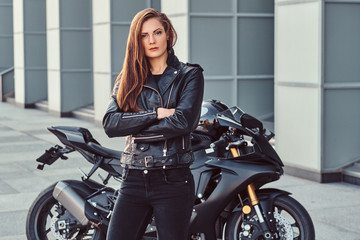 Wall Mural - A confident biker girl with her arms crossed next to her superbike outside a building.