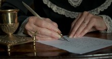 Lit By Natural Light The Aged Hands Of An Old Caucasian Woman From The Victorian Era Using An Ornate Inkwell And Dip Pen To Write A Letter.