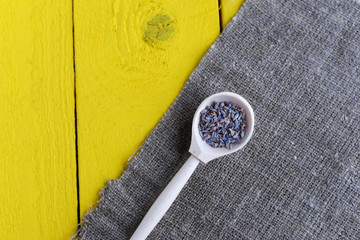 Wall Mural - wooden spoon with dried lavender flowers, linen napkin on a yellow rustic wooden table