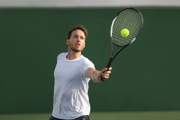 Tennis player man hitting ball playing tennis match on outdoor hard court in fitness club. Male sport athlete healthy lifestyle.