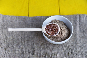 Wall Mural - bowl of flax flour, a spoon with flax seeds on a yellow wooden background and linen canvas