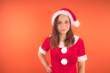 Wall Mural - Portrait of a young girl dressed as Santa Claus on orange background. Happy New year and merry Christmas!