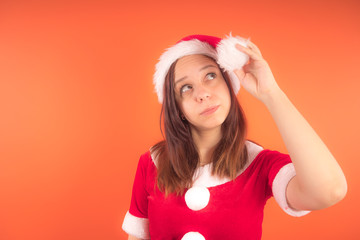 Wall Mural - Portrait of a young girl dressed as Santa Claus on orange background. Happy New year and merry Christmas!