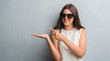 © Krakenimages.com - Young brunette woman over grunge grey wall wearing fashion sunglasses very happy pointing with hand and finger