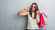 © Krakenimages.com - Young brunette woman over grunge grey wall holding colorful shopping bags with angry face, negative sign showing dislike with thumbs down, rejection concept