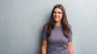 © Krakenimages.com - Young brunette woman over grunge grey wall wearing glasses with a happy face standing and smiling with a confident smile showing teeth