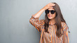 © Krakenimages.com - Young brunette woman over grunge grey wall wearing big sunglasses stressed with hand on head, shocked with shame and surprise face, angry and frustrated. Fear and upset for mistake.