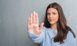 © Krakenimages.com - Young brunette woman over grunge grey wall with open hand doing stop sign with serious and confident expression, defense gesture
