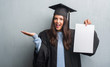 © Krakenimages.com - Young brunette woman over grunge grey wall wearing graduate uniform holding degree very happy and excited, winner expression celebrating victory screaming with big smile and raised hands