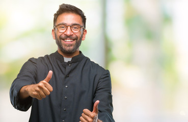 Adult hispanic catholic priest man over isolated background approving doing positive gesture with hand, thumbs up smiling and happy for success. Looking at the camera, winner gesture.