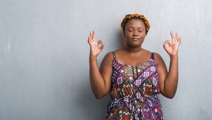 Sticker - Young african american woman over grey grunge wall wearing orange braids relax and smiling with eyes closed doing meditation gesture with fingers. Yoga concept.