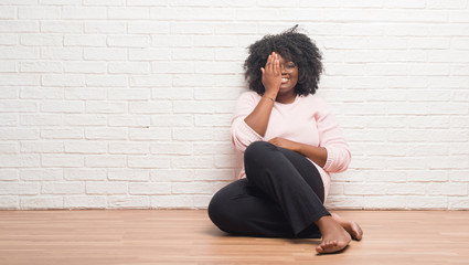 Poster - Young african american woman sitting on the floor at home covering one eye with hand with confident smile on face and surprise emotion.