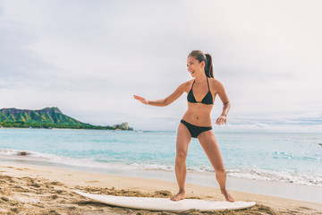 Wall Mural - Asian tourist woman on Hawaii beach learning to surf at surfing school in Waikiki, Honolulu, Oahu. Girl having fun practicing on surfboard on shore.