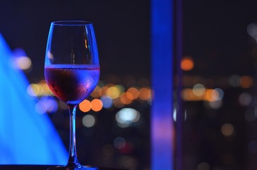 A glass of Rosé wine with bokeh light at Bangkok city and colorful light from rooftop building.