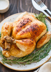 Wall Mural - Whole grill chicken with caramelized skin and fresh rosemary on a wooden dinner table.