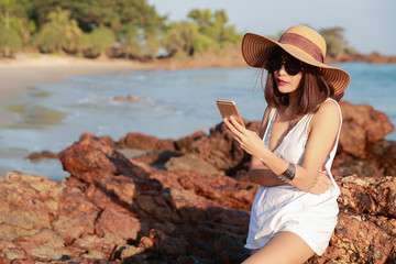 Wall Mural - beautiful and cute businesswoman using cell phone with sun glasses and hat on the beach during holiday vacation