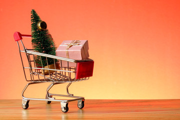 NEW YEAR CONCEPTUAL with shopping trolley,gift boxes and Christmas tree on a wooden table.